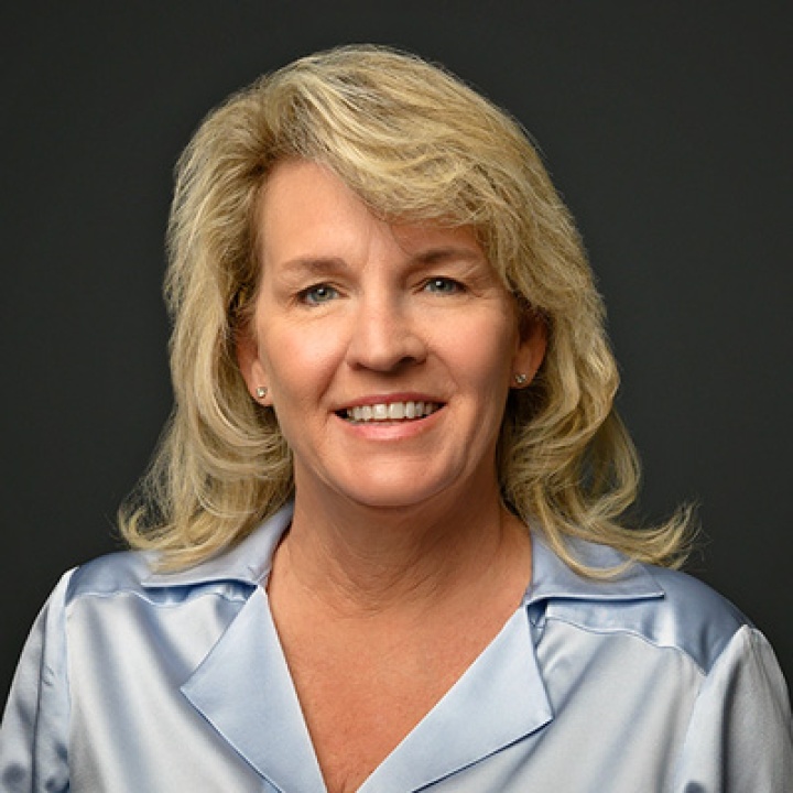 This is a headshot of Kelly Pruetz in a silver shirt on a gray background. 