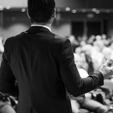 This image is black and white of a a man speaking in front of an audience