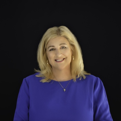 A picture of lisa higgins in a purple dress standing in front of a black wall.