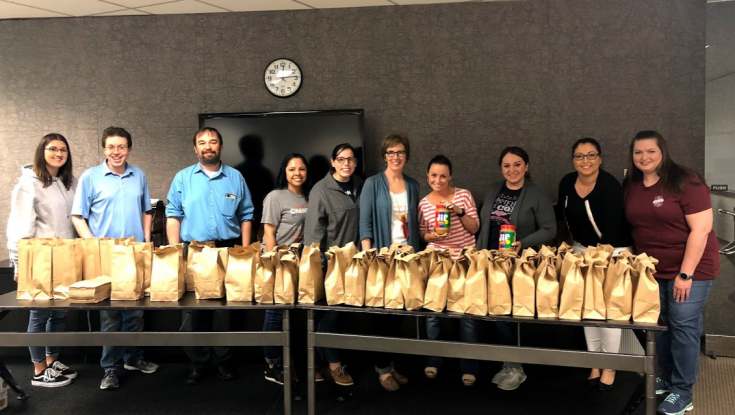 Group of employees standing in front of the sack lunches we made for the homeless