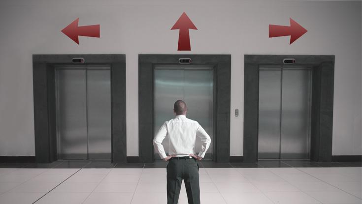 Man in front of an elevator bank with arrows in different directions above each elevator