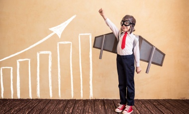 This is a photo of a little boy shooting for the sky along with a rising bar chart next to him
