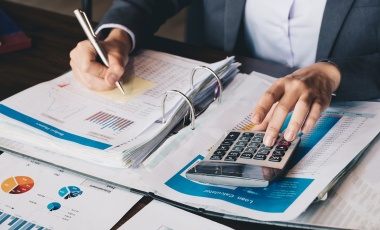 Photo of a person working on a calculator and writing in a notebook