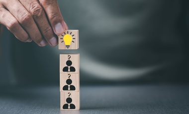 Man stacking wooden blocks with light bulb and people icons