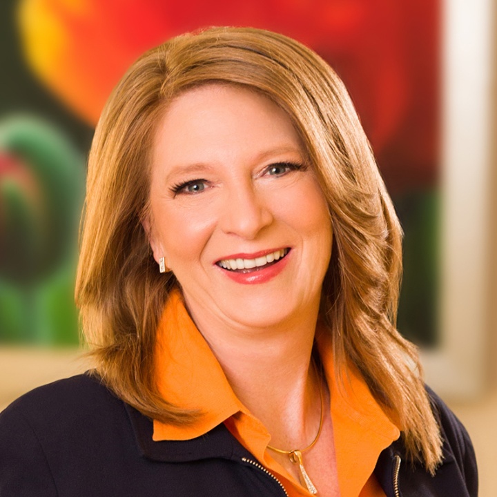 This is a picture of kate vitasek in a black suit and orange collared shirt. 