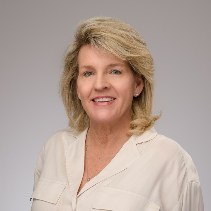 This is a headshot of Kelly Pruetz in an off white shirt on a gray background. 