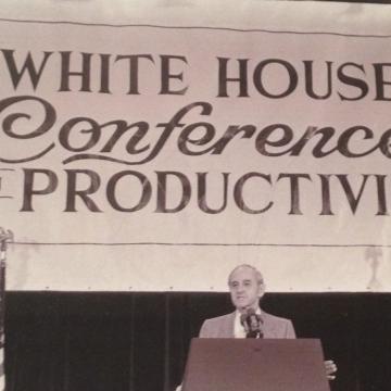A picture of the first White House Conference on Productivity with Jack Grayson at the podium