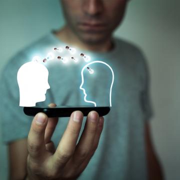 A picture of a man holding a hologram of two heads sharing information
