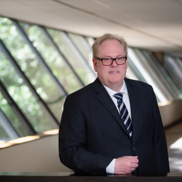 A picture of Anthony Marshall in a black suite standing inside the APQC Headquarters in front of a window