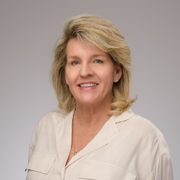 This is a headshot of Kelly Pruetz in an off white shirt on a gray background. 