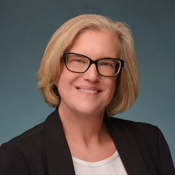 A picture of Laura Clymer against a Gray background as she wears a black vneck shirt and black glasses.