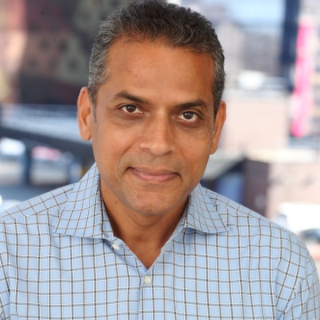 Headshot of Atul Vashistha, Founder and Chairman of Neo Group in a blue checkered shirt, smiling slightly with a blurred city background.